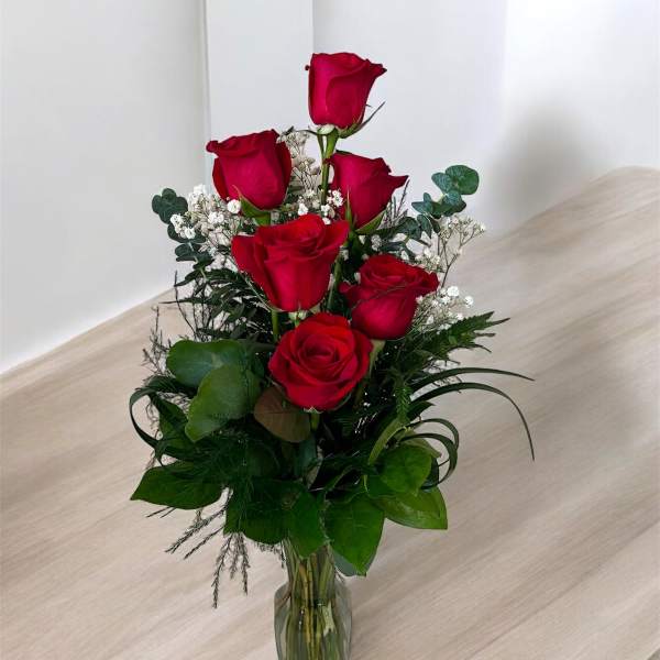 Red roses arranged in a clear glass vase with white filler flowers