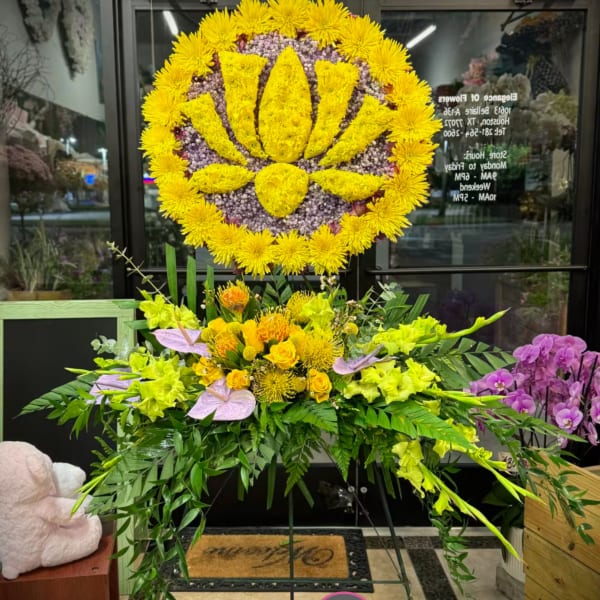 Large yellow floral standing spray with a circular emblem and mixed blooms below