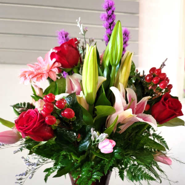 Mixed bouquet of lilies, roses, and pink daisies in a red glass vase