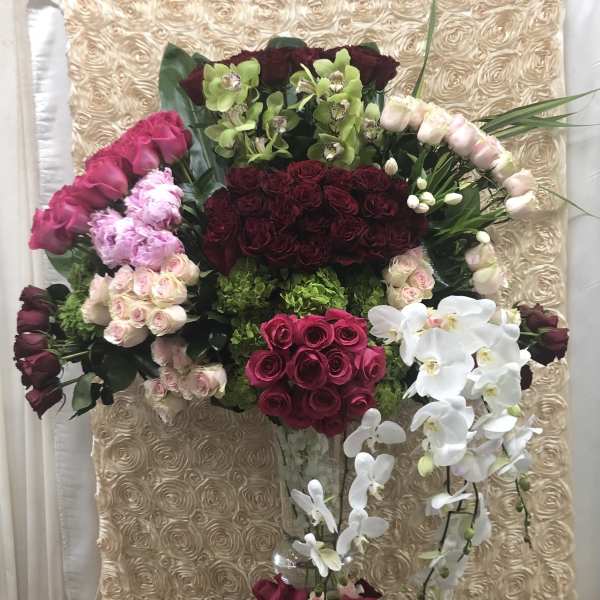 Large floral arrangement with roses and orchids in a clear vase