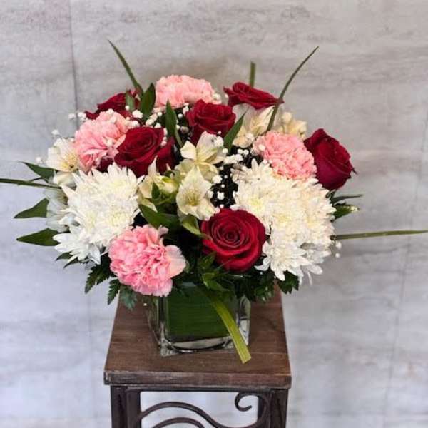Bouquet of red roses, pink carnations, and white chrysanthemums in a glass vase