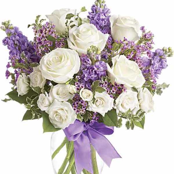 White roses and purple flowers in a clear glass vase with a lavender ribbon