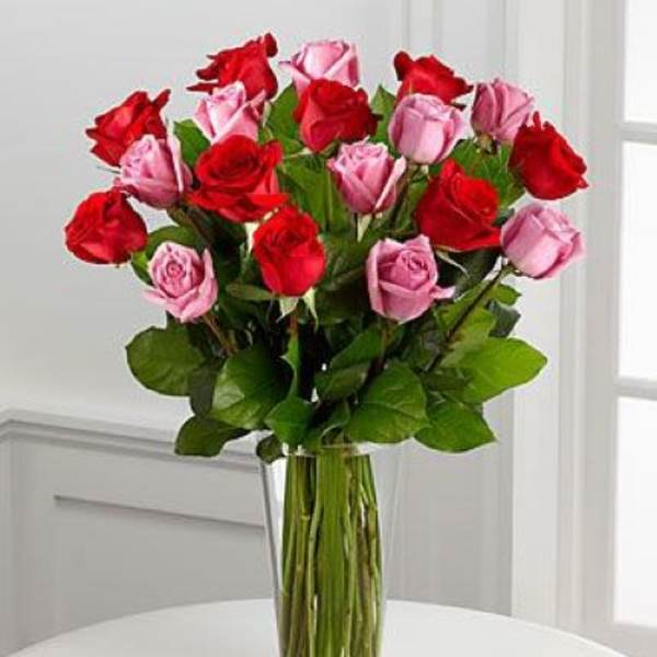 Tall bouquet of red and pink roses arranged in a clear glass vase on a white table