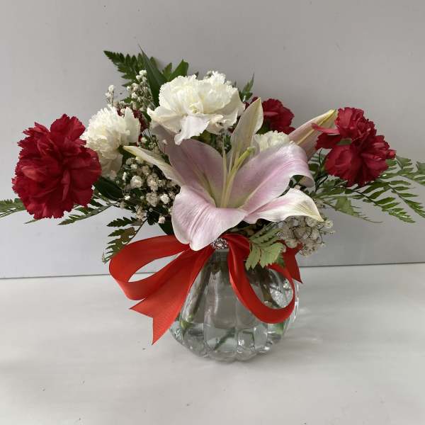 Pink lily and red-white carnations in a glass vase with a red ribbon