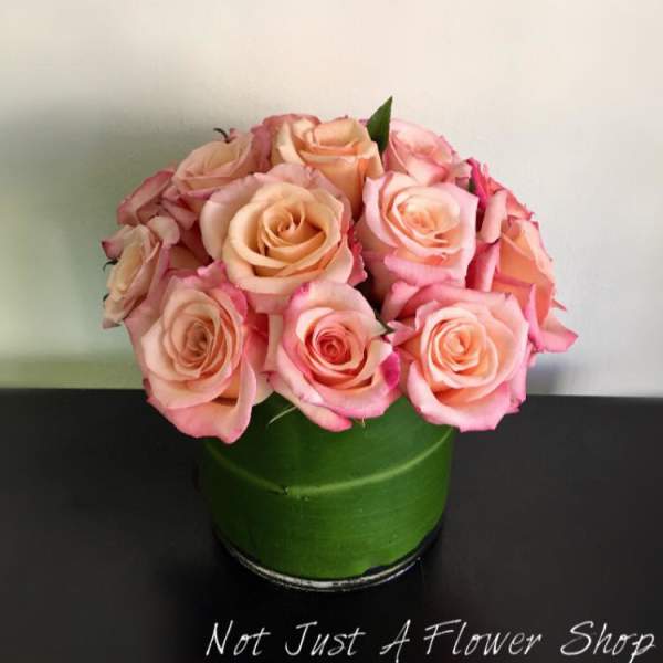 Pink and peach roses arranged in a green round box