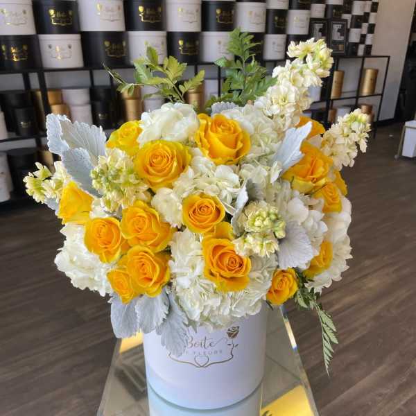Yellow roses and white blooms arranged in a white hatbox