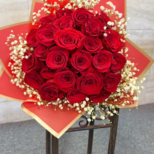 Round bouquet of red roses with white filler flowers wrapped in red and gold paper.