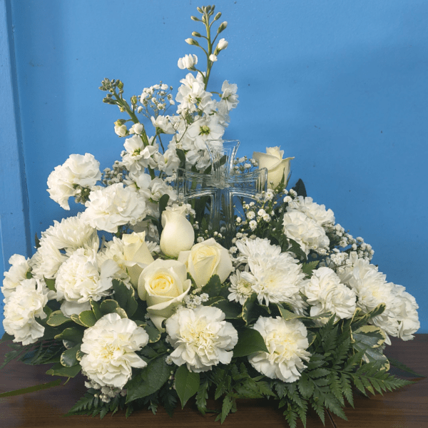 White roses, carnations, and mums arranged around a clear glass cross.