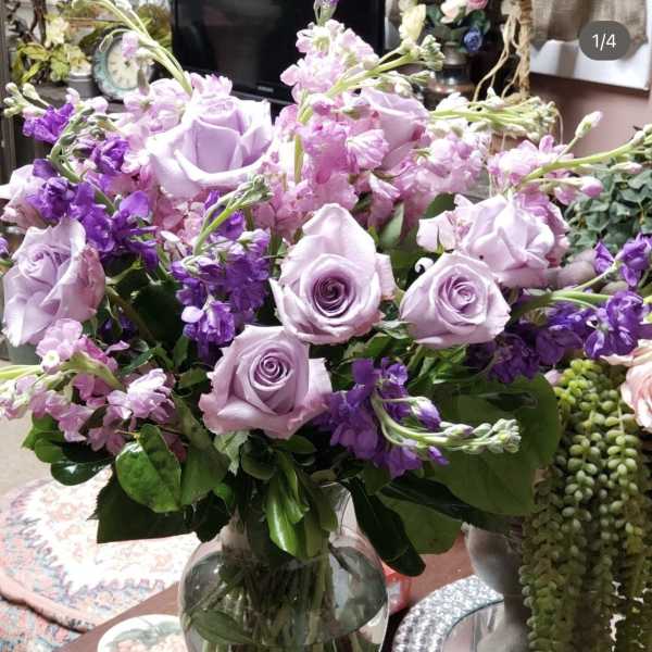 Lavender roses and purple flowers arranged in a clear glass vase