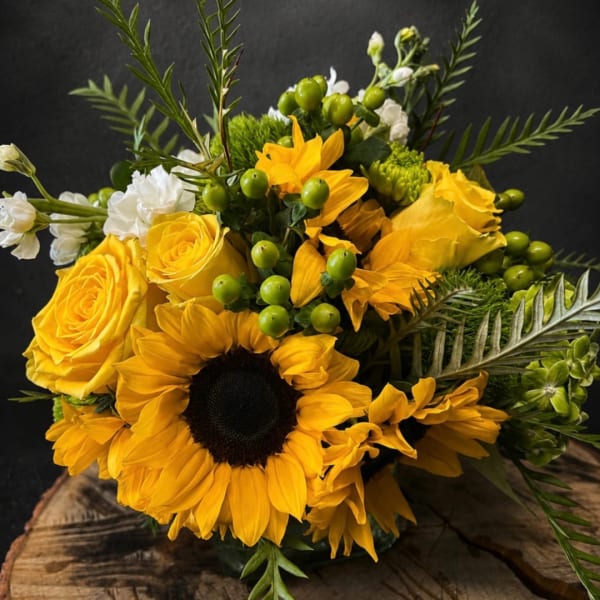 Yellow sunflowers and roses arranged with white blooms and green berries