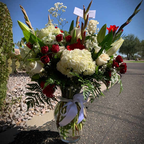 Large bouquet of red and white flowers in a glass vase with a white ribbon