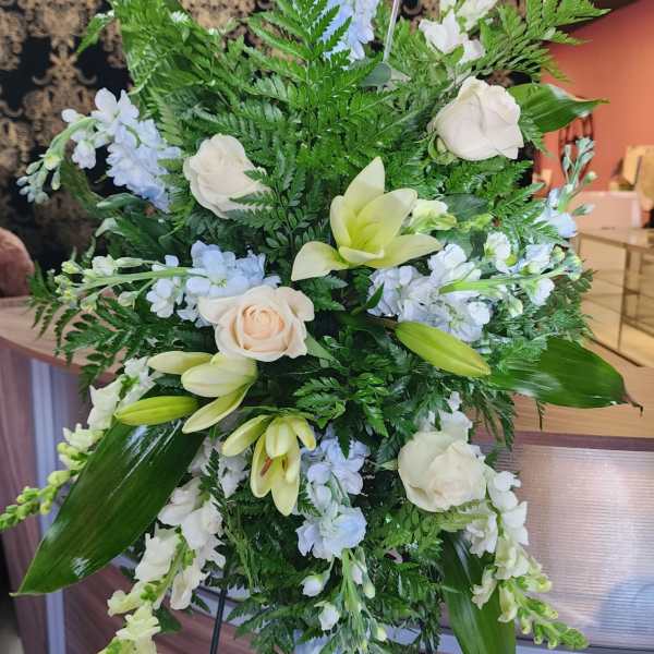 Standing floral spray with white roses, lilies, and pale blue blooms