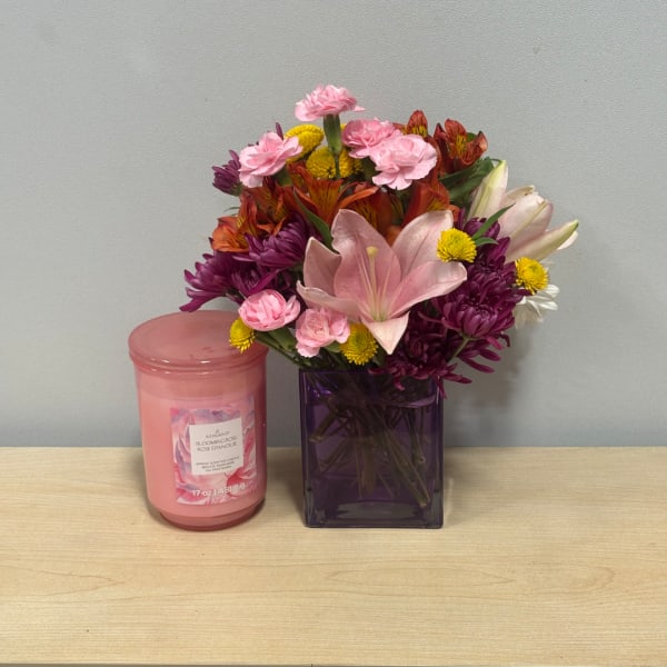 Mixed bouquet in a purple vase beside a pink candle jar