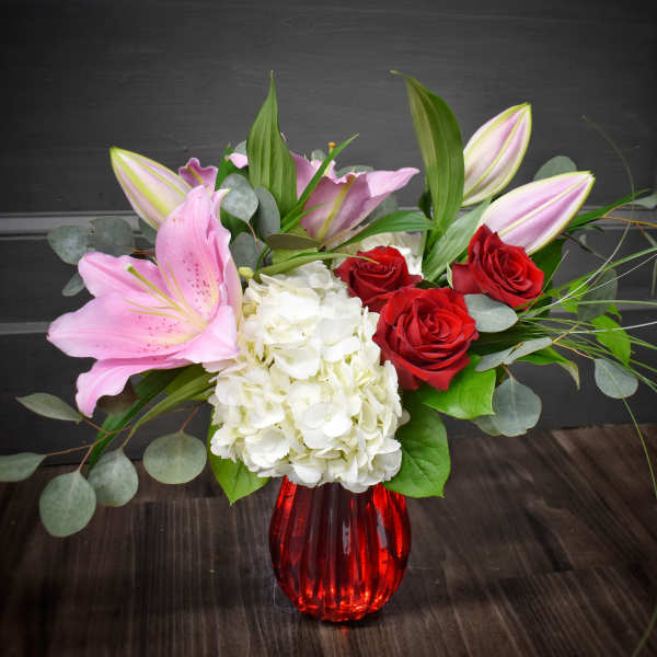 Pink lilies, red roses, and white hydrangea in a red vase