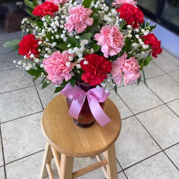 Pink and red carnations in a glass vase with a pink ribbon
