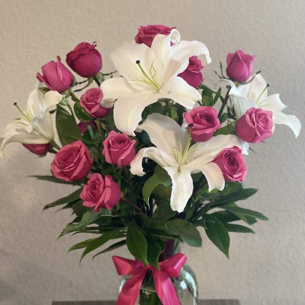 Pink roses and white lilies in a glass vase with a pink ribbon