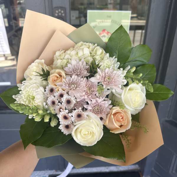 Hand-tied bouquet of white and blush flowers wrapped in tan paper