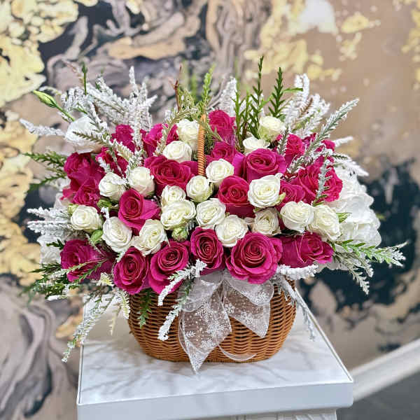 Basket of pink and white roses with frosted greenery and a ribbon bow