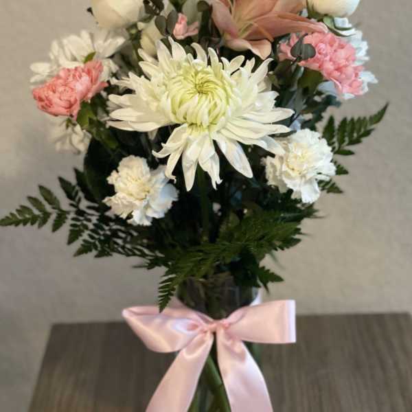 Bouquet of white and pink flowers in a glass vase with a pink ribbon