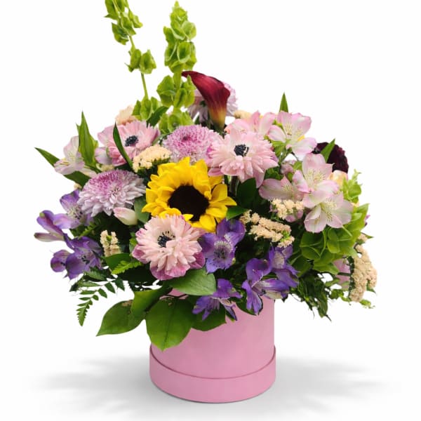 Mixed bouquet in a pink round box with a sunflower and pastel blooms