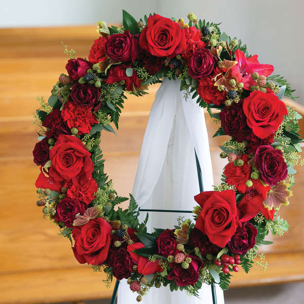 Red rose wreath on a white stand with a ribbon drape