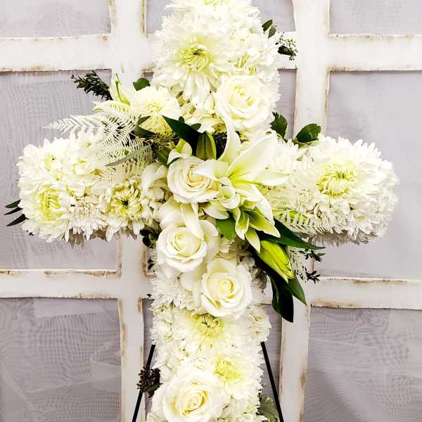 White floral cross on a stand with roses and chrysanthemums