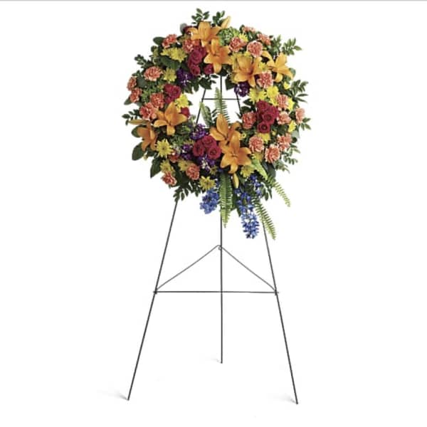 Large floral wreath on a standing easel with mixed orange, pink, purple, and yellow flowers