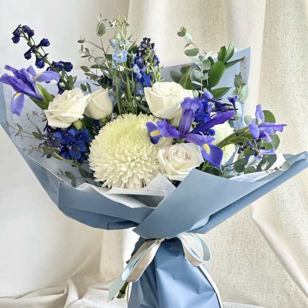 Bouquet of white roses and purple irises wrapped in blue paper