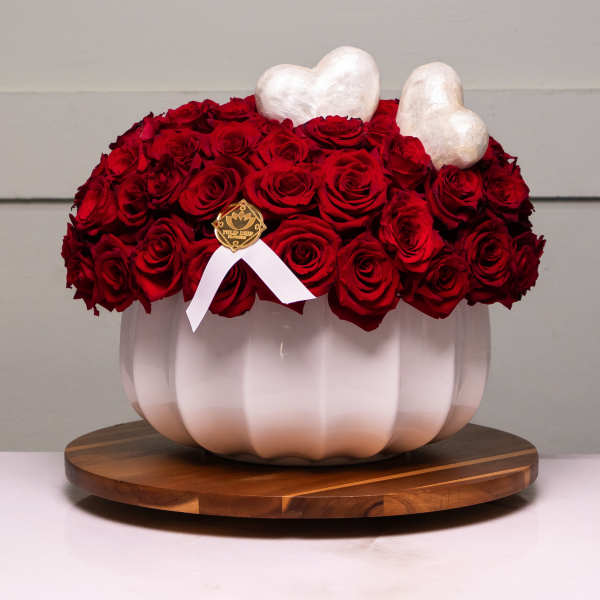 Red rose arrangement in a white pumpkin-shaped vase with heart accents