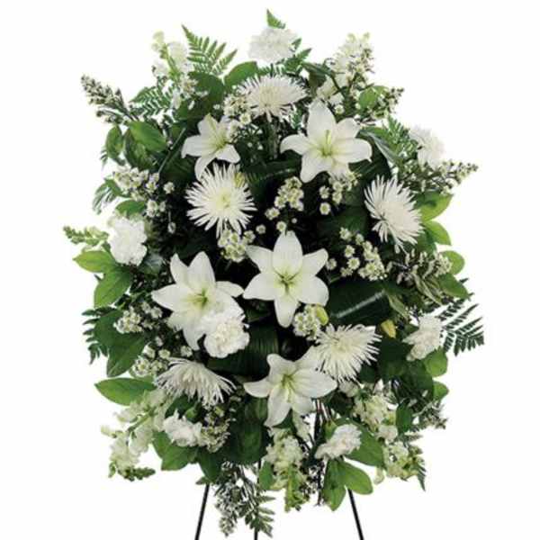 Standing spray of white lilies, carnations, and mums with small white fillers and lush greenery on an easel.
