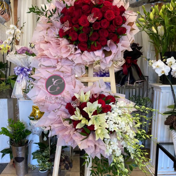 Large standing floral display with red roses, white orchids, and pink wrapping