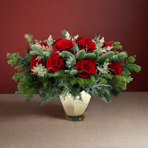 Red roses arranged in a clear vase with evergreen accents