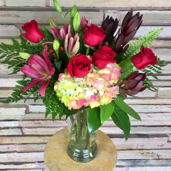 Bouquet of red roses, lilies, and hydrangea in a glass vase