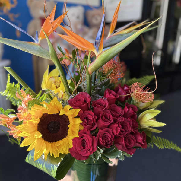 Tropical arrangement with birds of paradise, red roses, sunflower and lilies in a glass vase