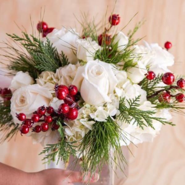 White rose bouquet with red berries and greenery in a clear vase