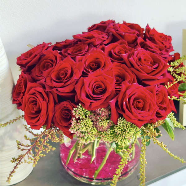 Red roses arranged in a clear glass vase with small green filler flowers