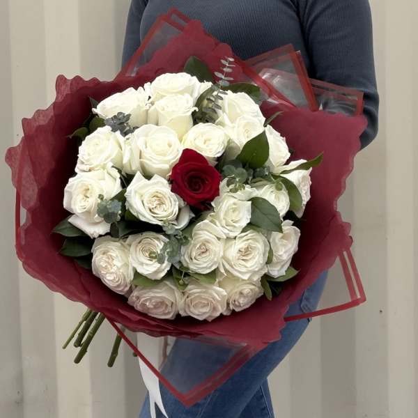 Bouquet of white roses with one red rose wrapped in burgundy paper