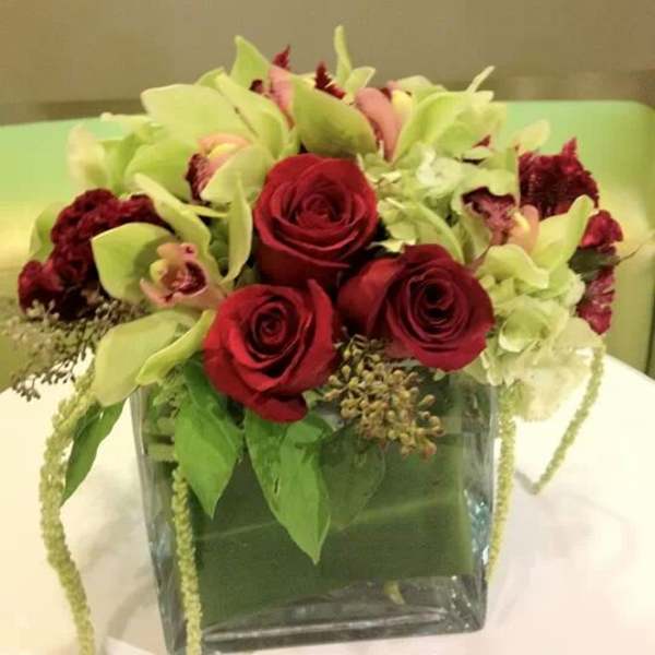 Red roses and pale green orchids in a square glass vase