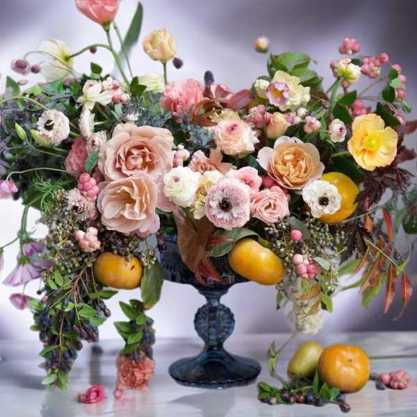 Mixed pastel floral arrangement in a dark blue pedestal vase with fruit accents