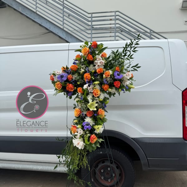 Large floral cross arrangement with orange, white, and purple flowers on a stand