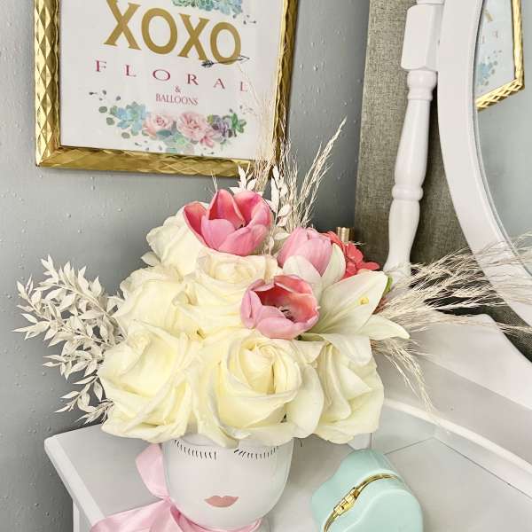 Pink and white flower arrangement in a face-shaped vase with a ribbon