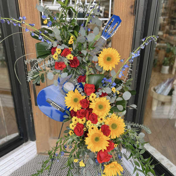 Floral arrangement shaped with a blue guitar and bright sunflowers and roses