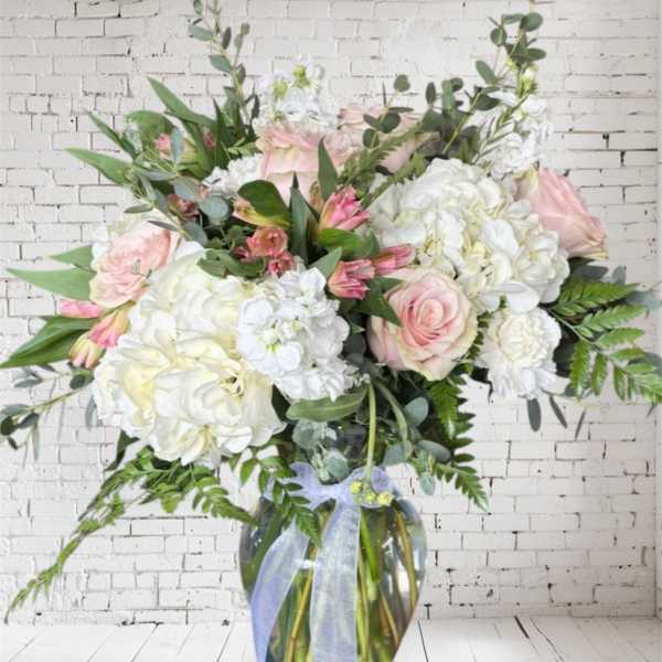 Large bouquet of pink and white flowers in a glass vase with a ribbon
