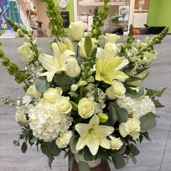 White lilies and roses arranged in a tall vase with greenery