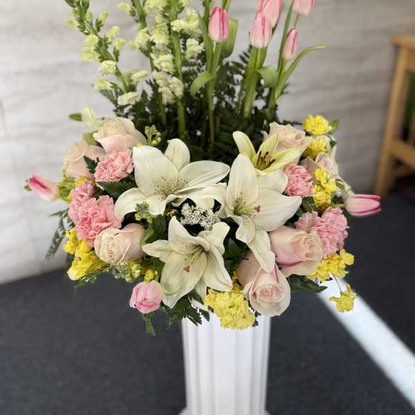 Pink tulips, white lilies, and roses in a tall white vase