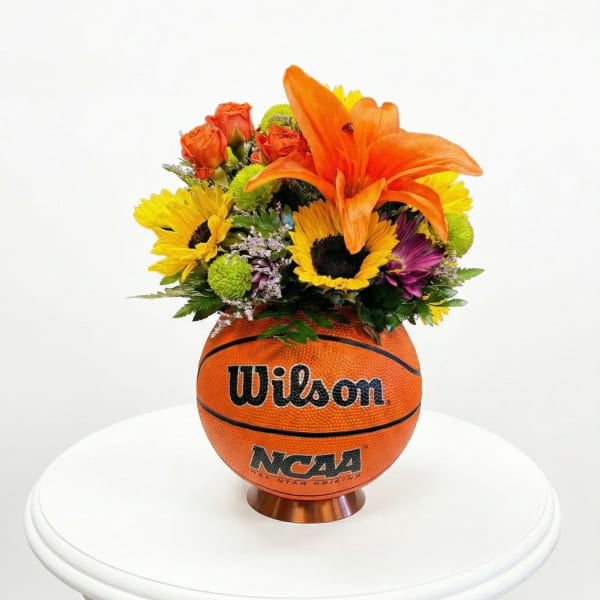 Flower arrangement in a basketball-shaped container with orange lilies and sunflowers