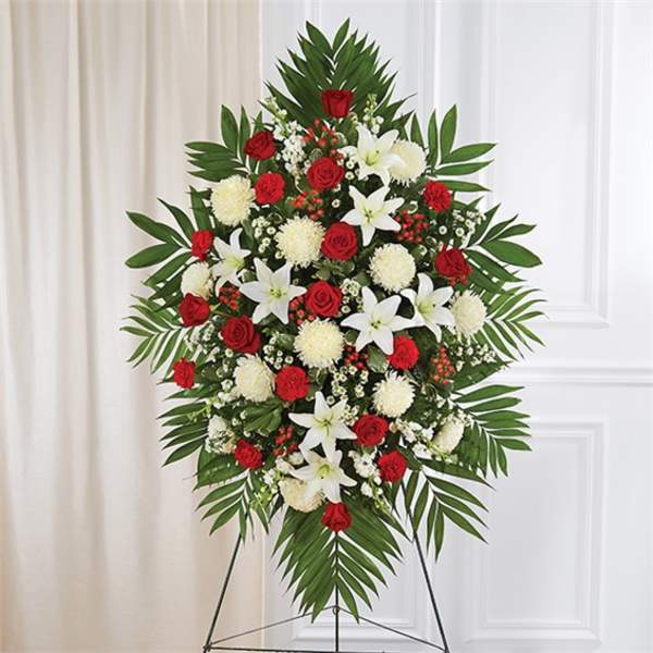 Tall standing spray of red roses, white lilies, and white mums on a metal easel.