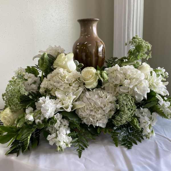 White floral arrangement with roses and hydrangeas around a brown vase