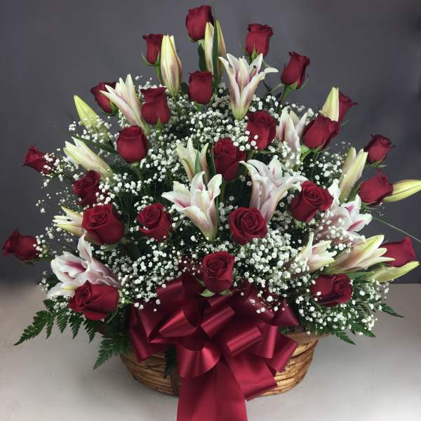 Basket arrangement of red roses and white lilies with a burgundy ribbon