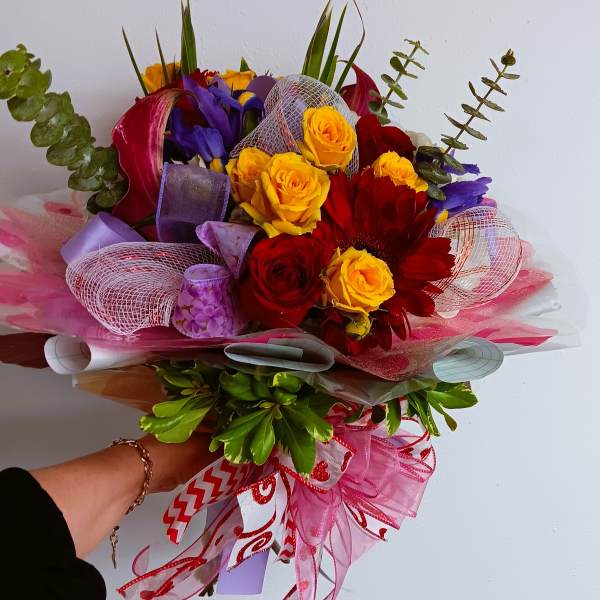 Handheld bouquet of red, yellow, and purple flowers with pink ribbon wrap
